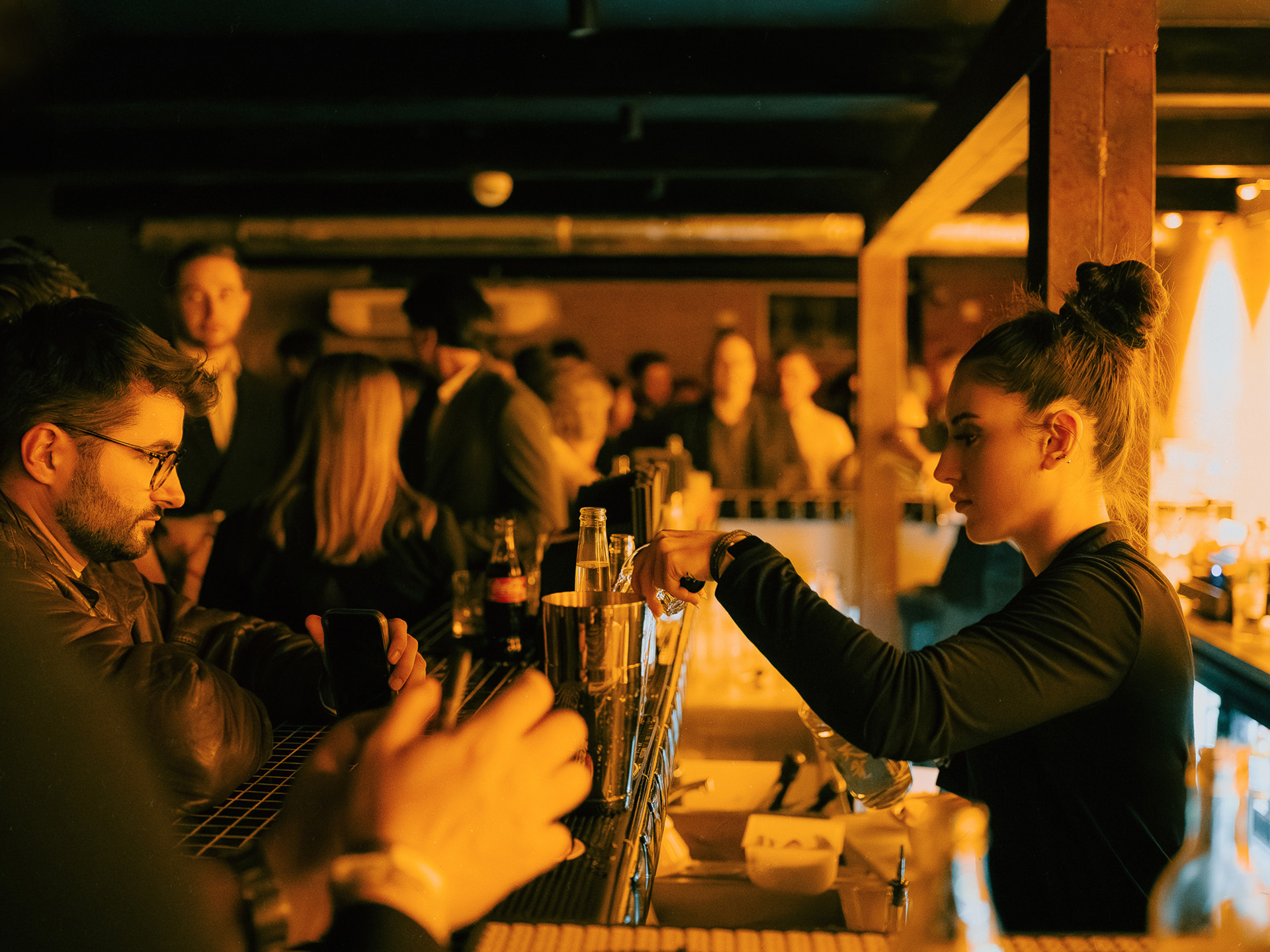 Bar podczas dużego eventu firmowego – barmanka przygotowuje drinki, goście w tle